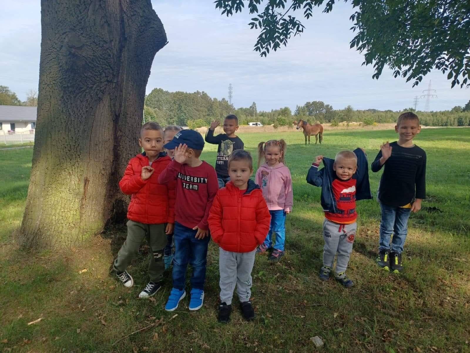 Dzieci stoją w grupie obok drzewa.
