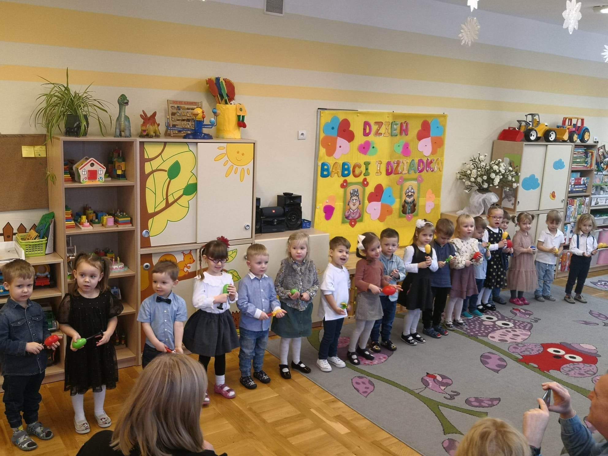Dzieci stoją w p&oacute;łkolu i śpiewają piosenki dla babci i dziadka.