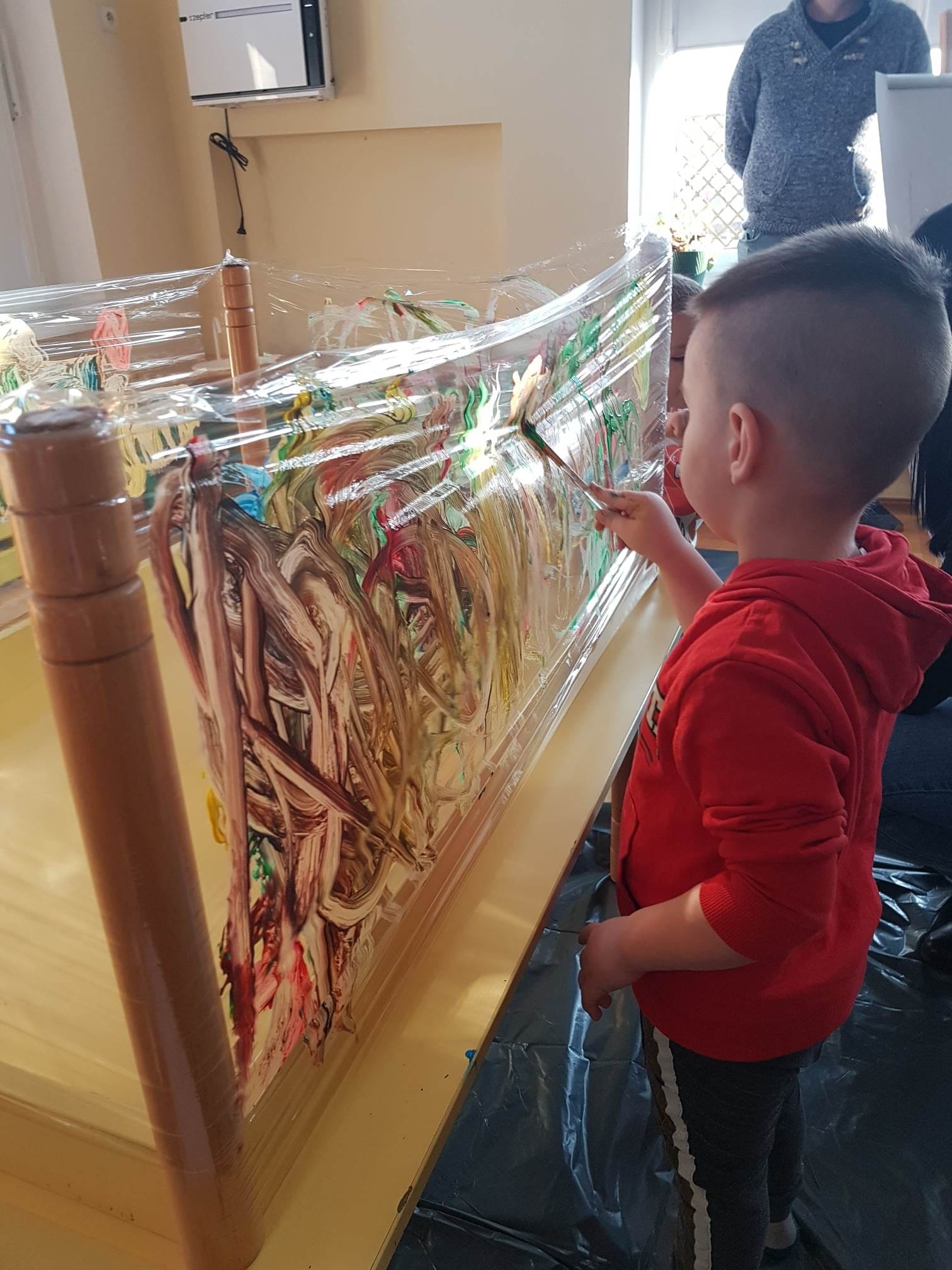 Chłopiec maluje farbami na folii.