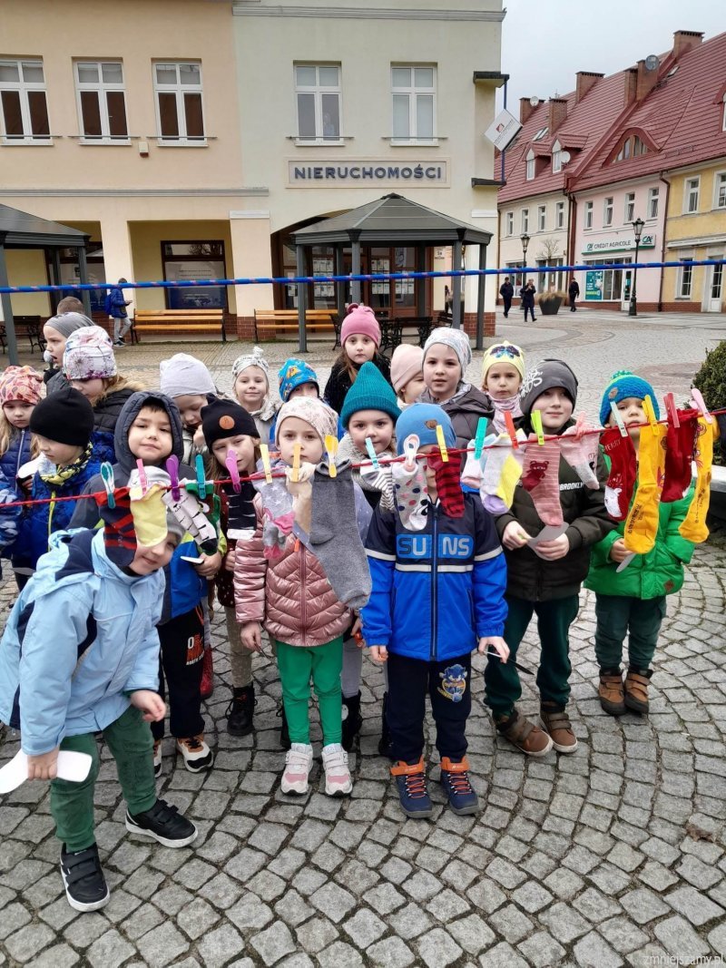 Dzieci stoją na Rynku przed nimi sznurek z przypiętymi skarpetkami