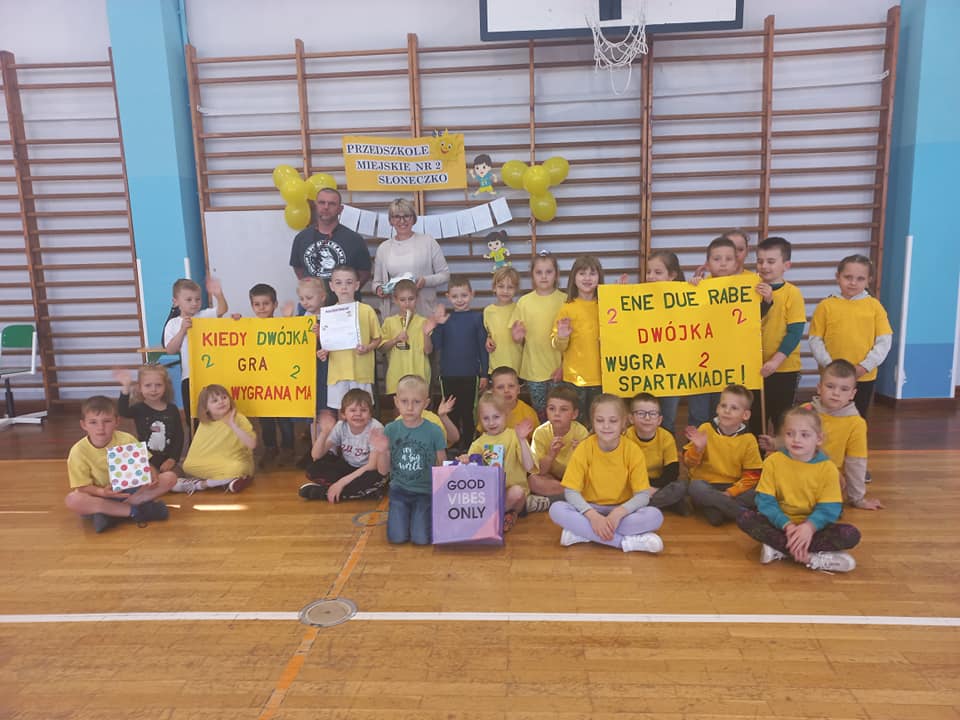 Dzieci ubrane w stroje sportowe pozują do zdjęcia. Jedno dziecko trzyma w ręku puchar.