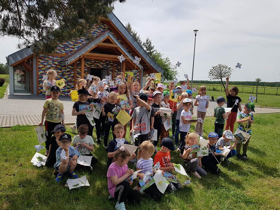 Dzieci stoją w grupie na trawie trzymają w ręku papierowe wiatraki.