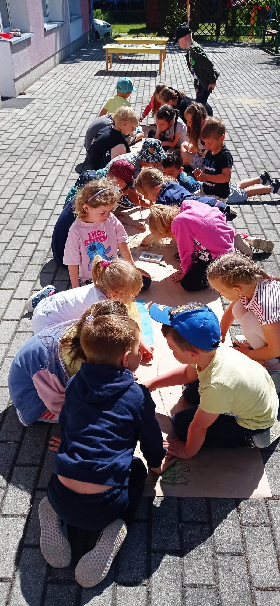 Dzieci są na dworze i rysują na szarym papierze.