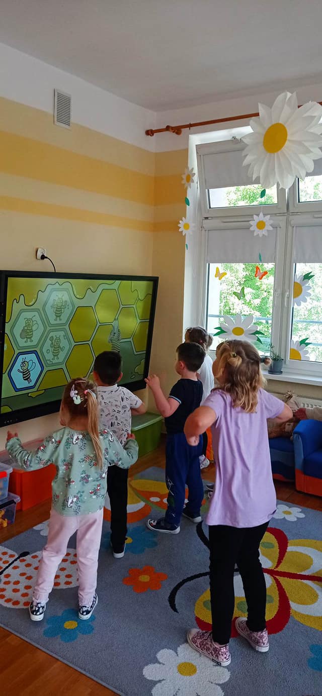 Dzieci ćwiczą przed tablicą interaktywną.