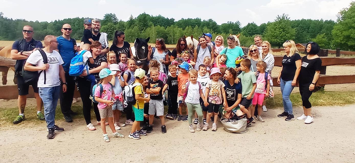 Dzieci wraz z rodzicami stoją w grupie na powietrzu.