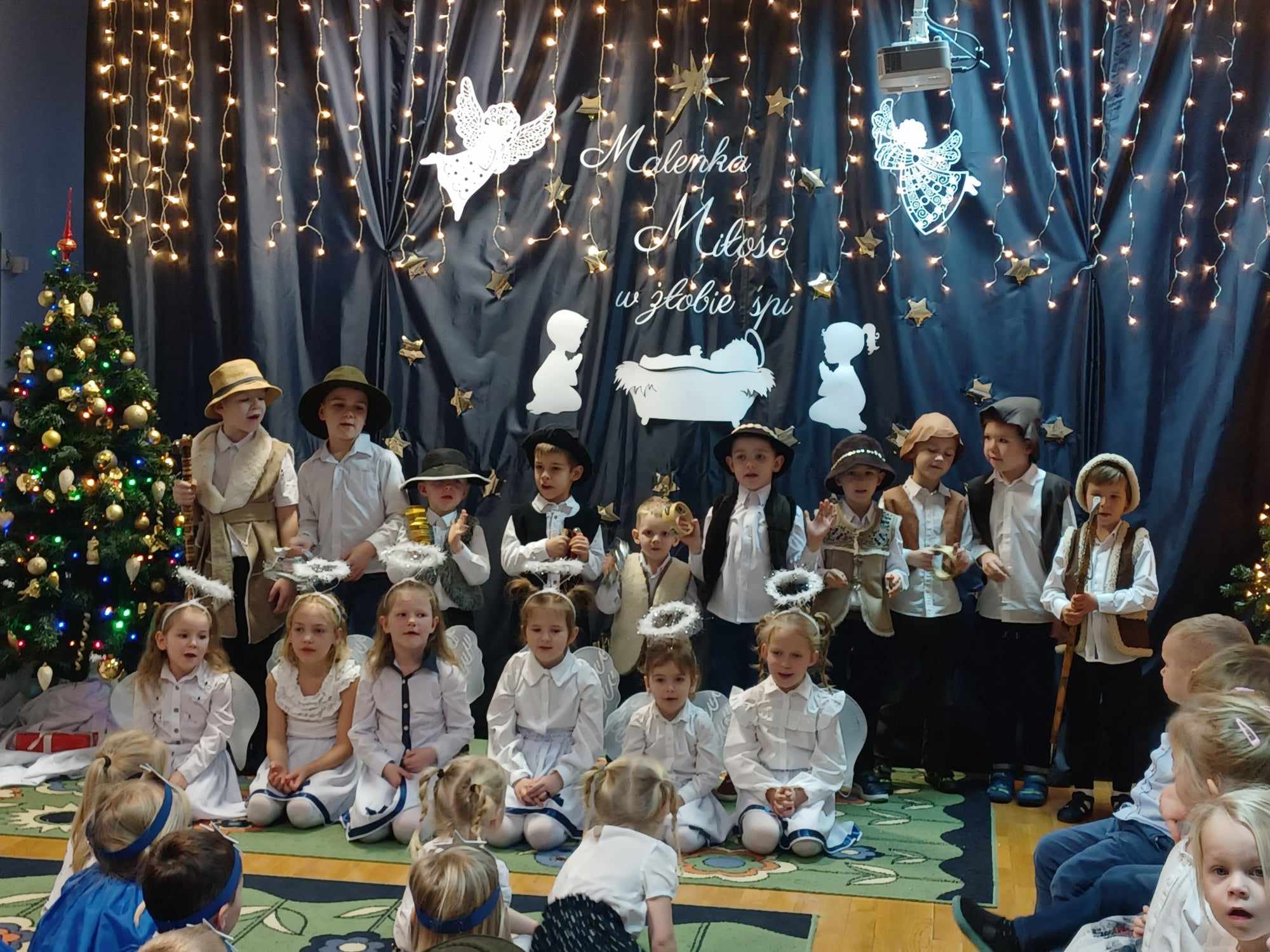 Dzieci przebrane za anioły i pastuszk&oacute;w stoją i śpiewają kolędy.