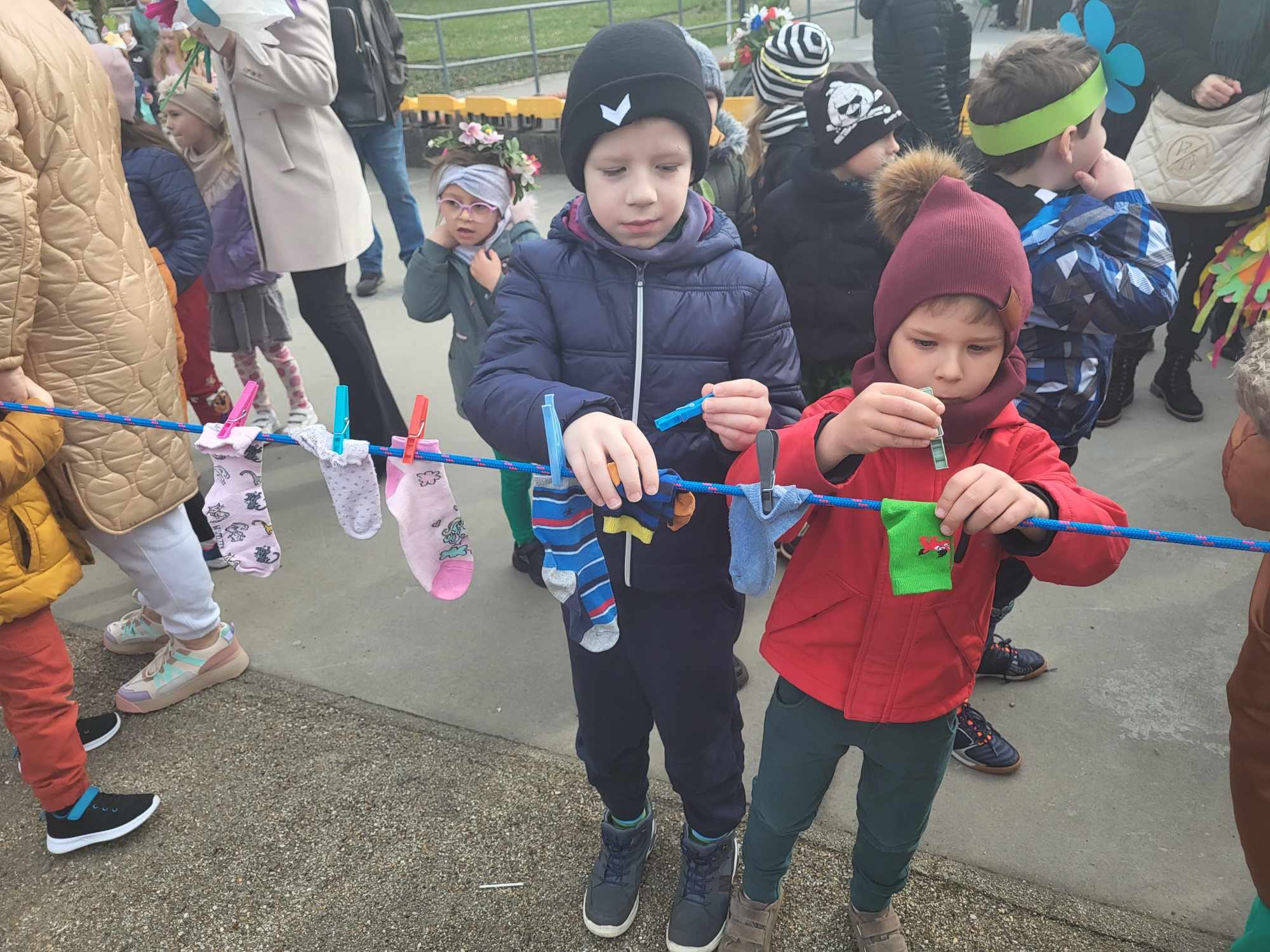 Dw&oacute;ch chłopc&oacute;w przyczepia skarpetki do sznurka na rynku.