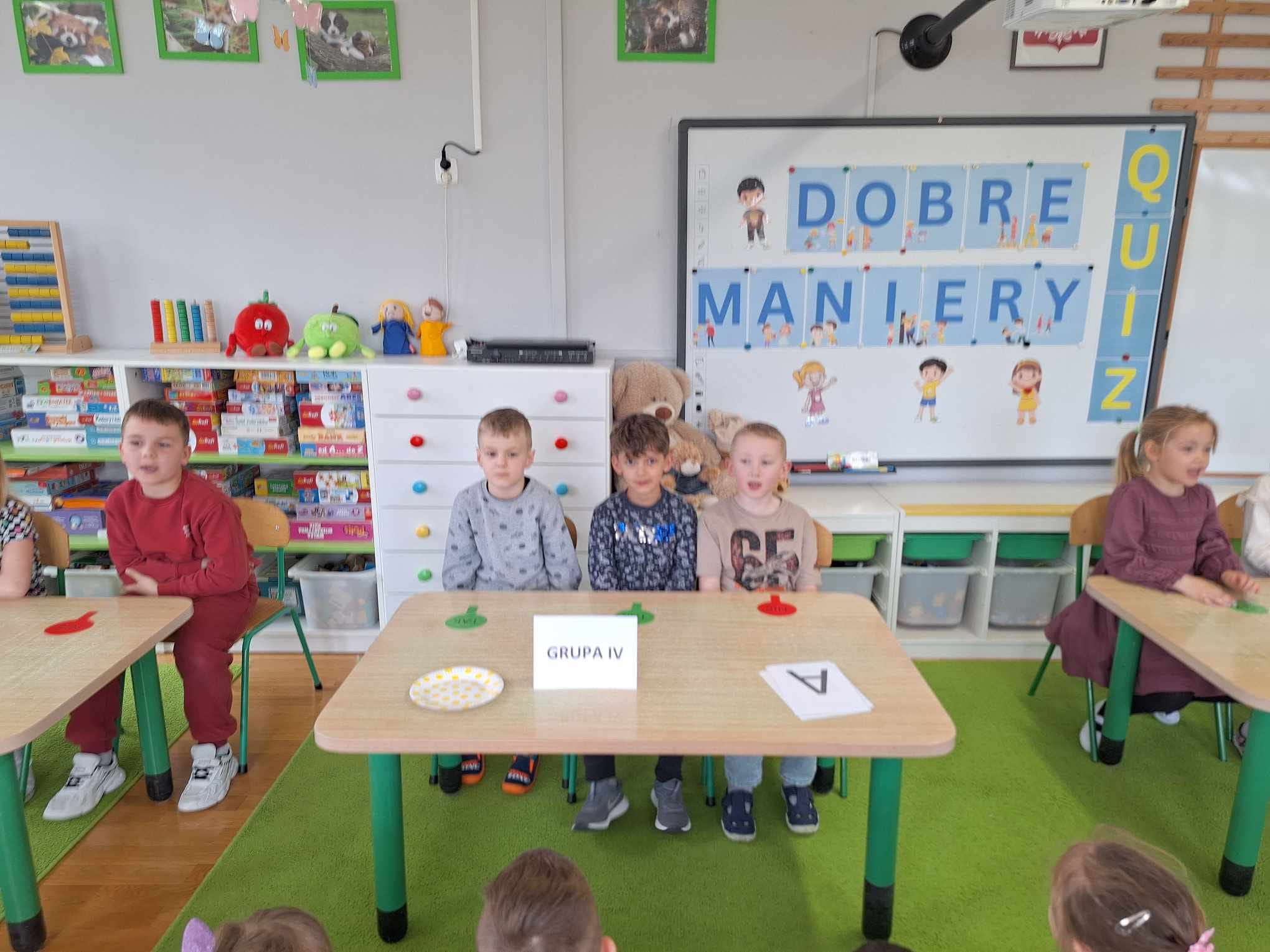 Dzieci siedzą przy stolikach i biorą udział w quizie.