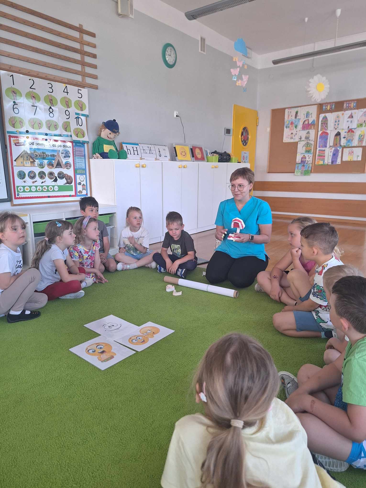 Pani higienistka siedzi z dziećmi na dywanie.