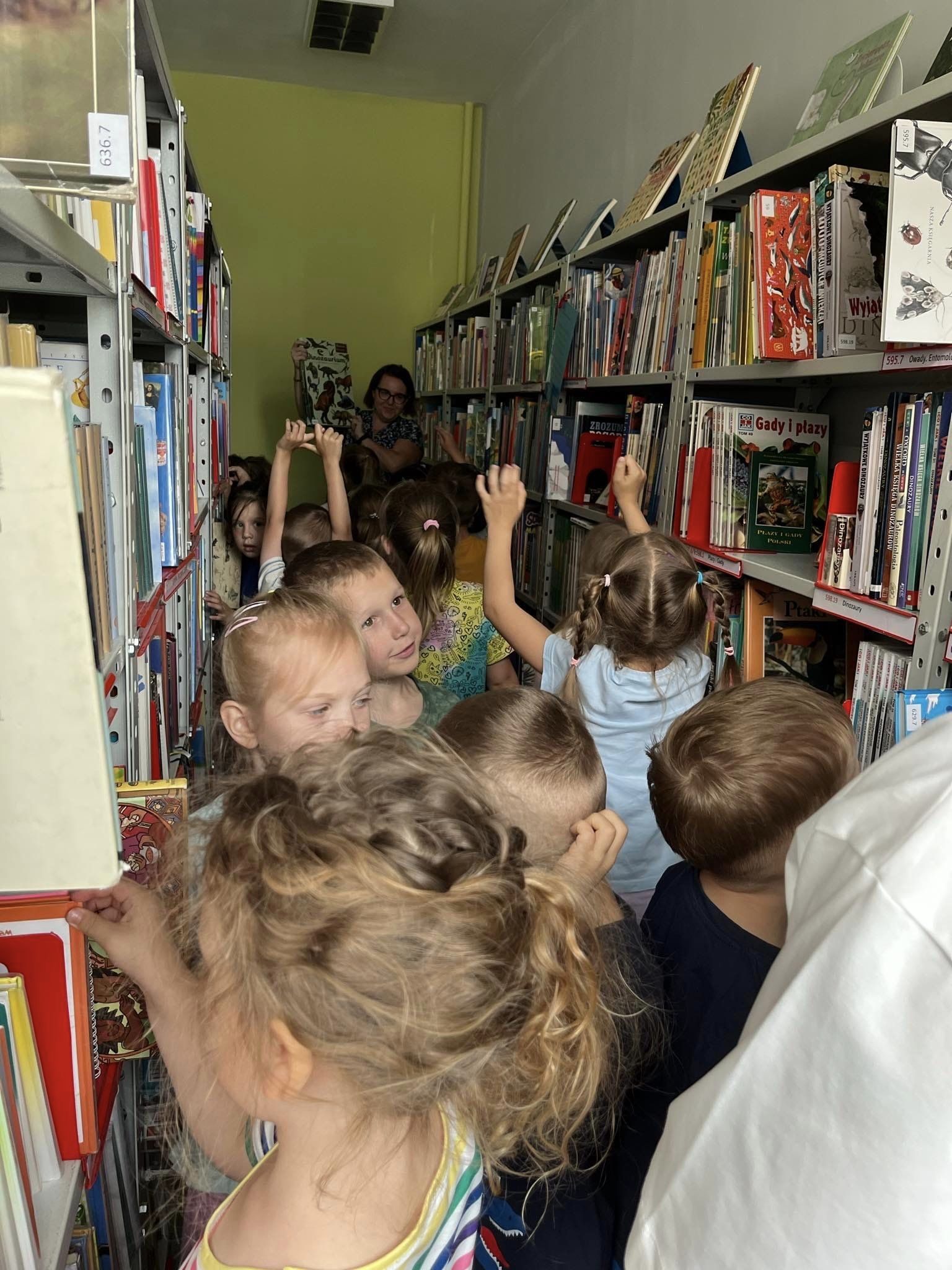 Dzieci stoją pomiędzy regałami z książkami w bibliotece.