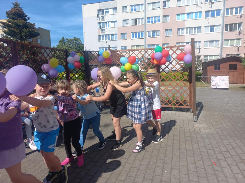 Dzieci tańczą ustawione w pociąg w ogrodzie przedszkolnym.