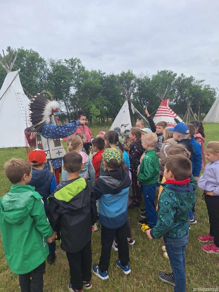 Dzieci stoją przy namiotach indiańskich i słuchają indianina.