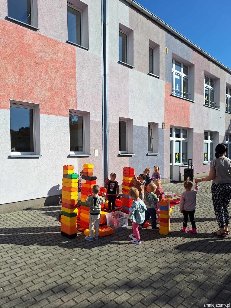 Dzieci bawią się na tarasie przedszkolnym dużymi klockami.