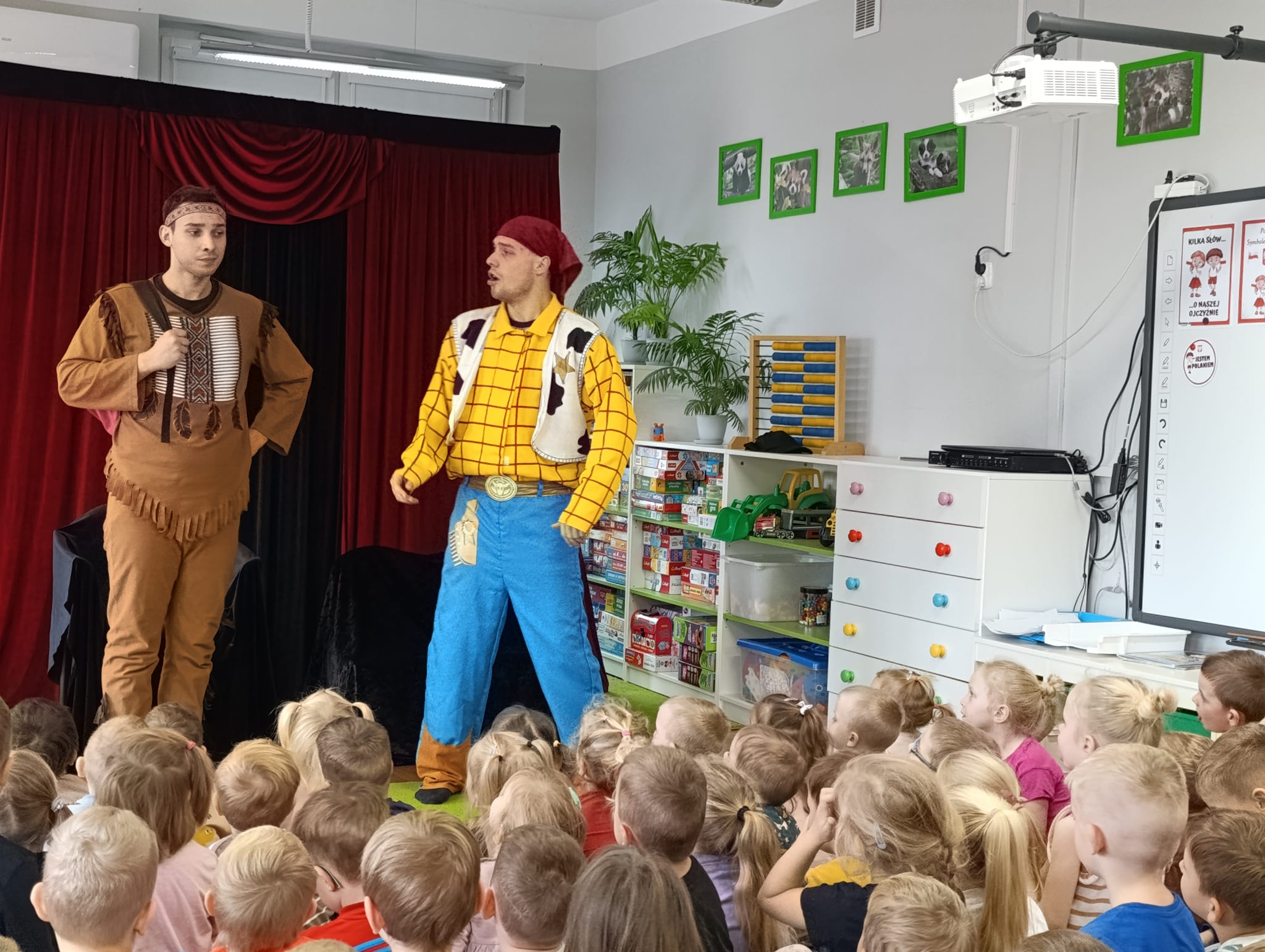 Dzieci siedzą na dywanie i oglądają teatrzyk w wykonaniu kowboja i kota.