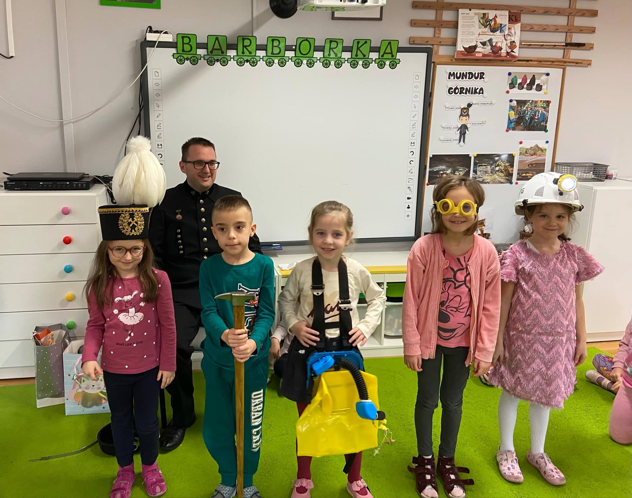 Czworo dzieci stoi w g&oacute;rniczych czapkach razem z g&oacute;rnikiem.