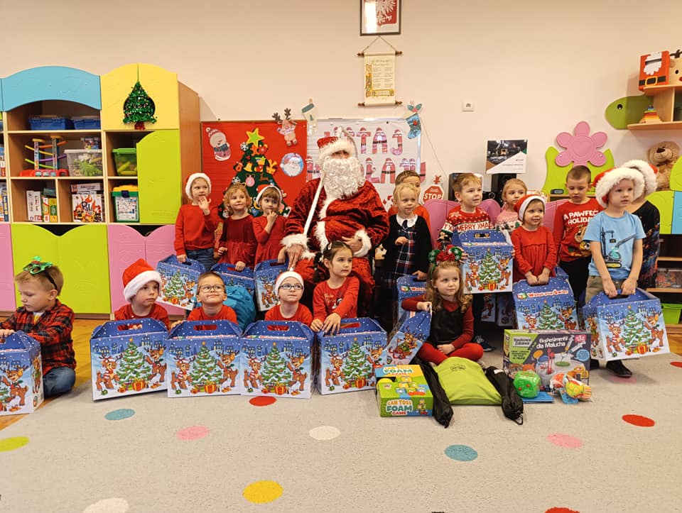 Dzieci ubrane na czerwono, trzymają w ręku paczki, pozują do zdjęcia z mikołajem