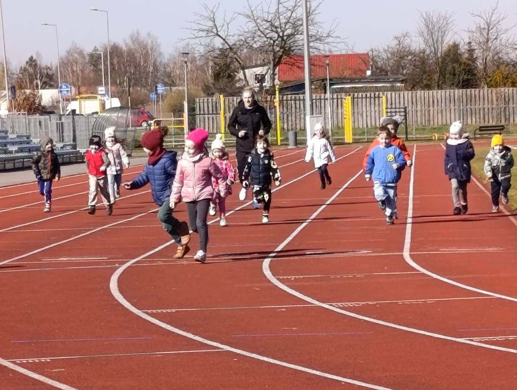 Dzieci biegną na stadionie po torze.