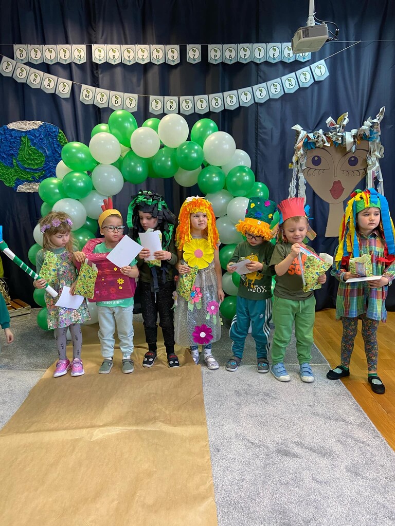 Dzieci ubrane w stroje zrobione z surowc&oacute;w wt&oacute;rnych stoją w rzędzie z dyplomami i upominkami.i 