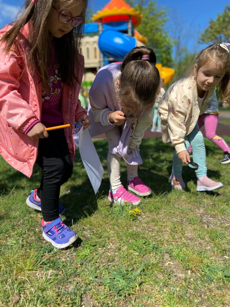 Trzy dziewczynki szukają z lupami owad&oacute;w na trawie.