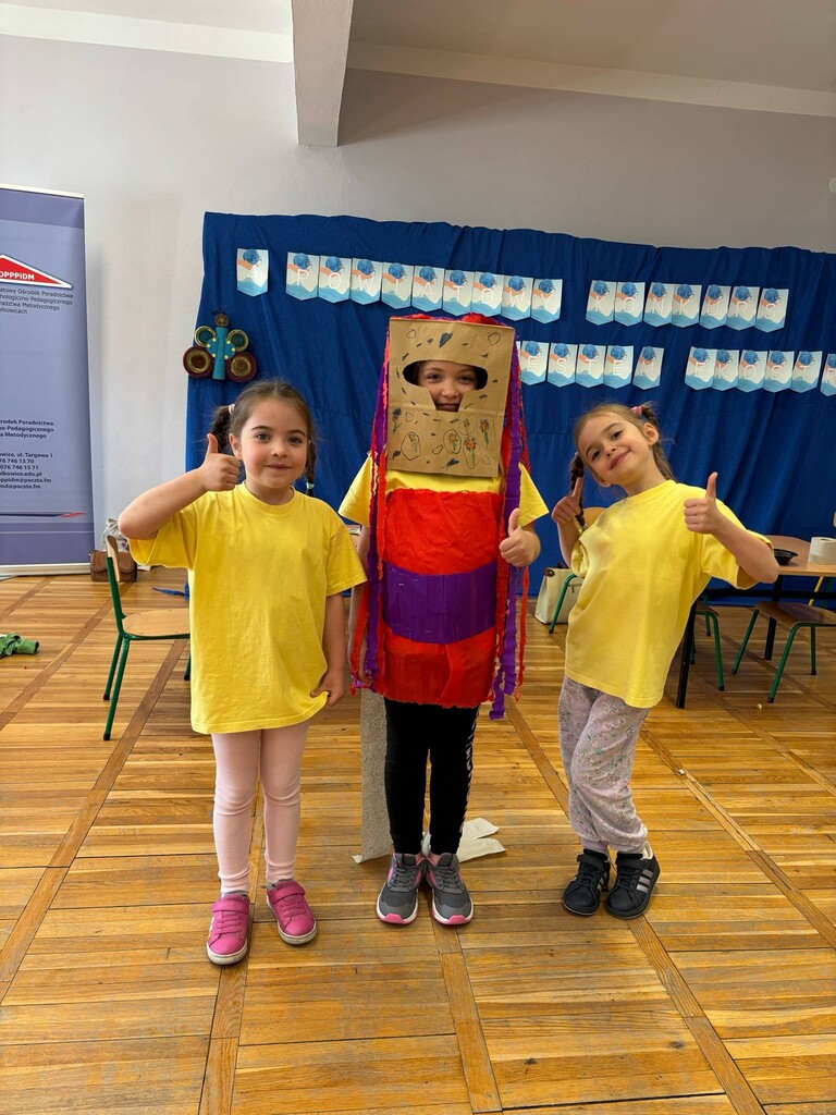 Dwoje dzieci stoi ubranych w ż&oacute;łte koszulki jedno dziecko ma str&oacute;j zrobiony z kartonu.