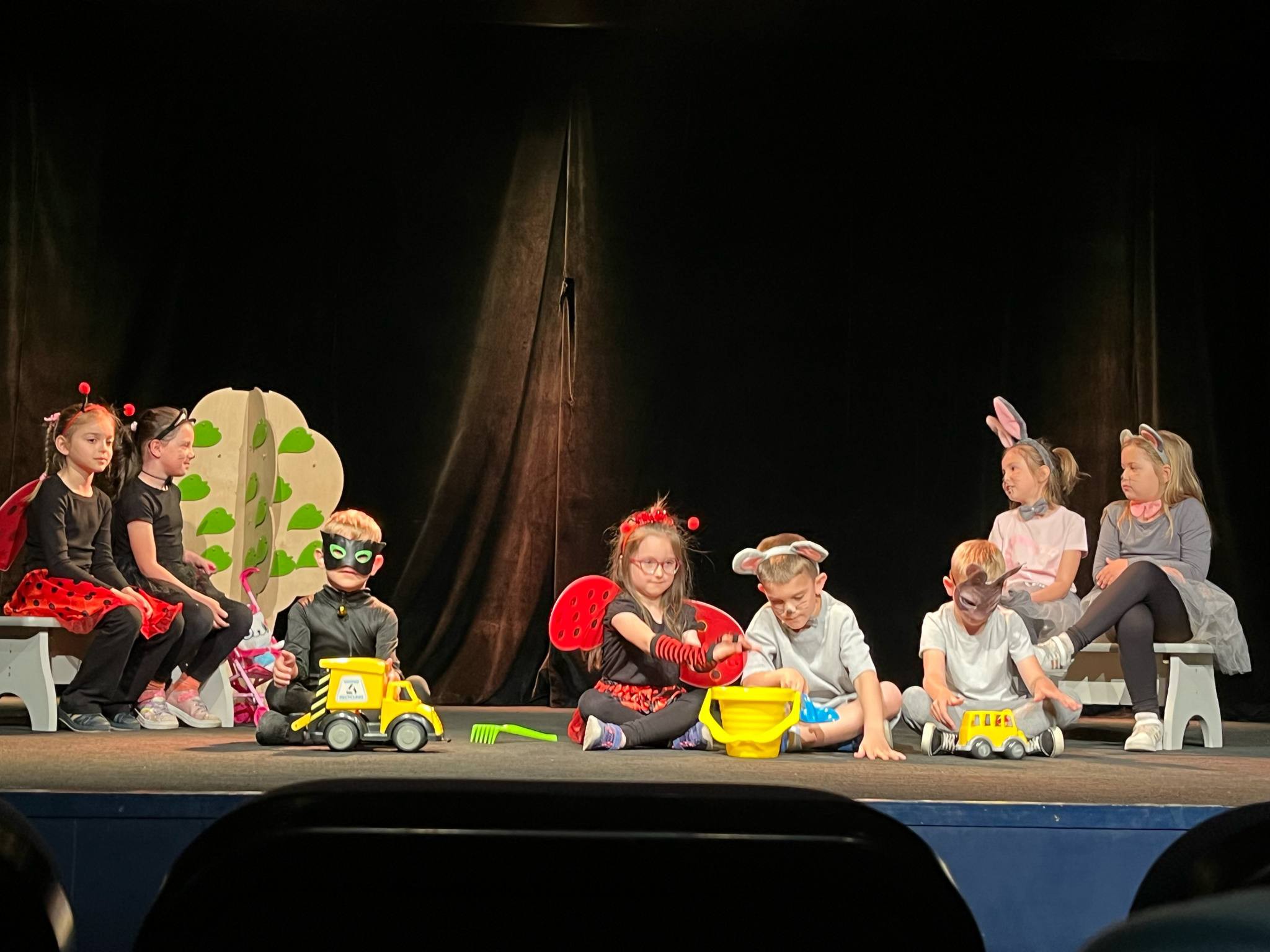 Dzieci przebrane za koty i biedronki oraz bawiące się samochodami występują na scenie.