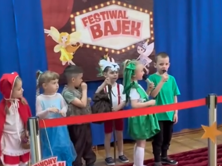 Dzieci przebrane za postacie z bajek stoją na czerwonym dywanie.