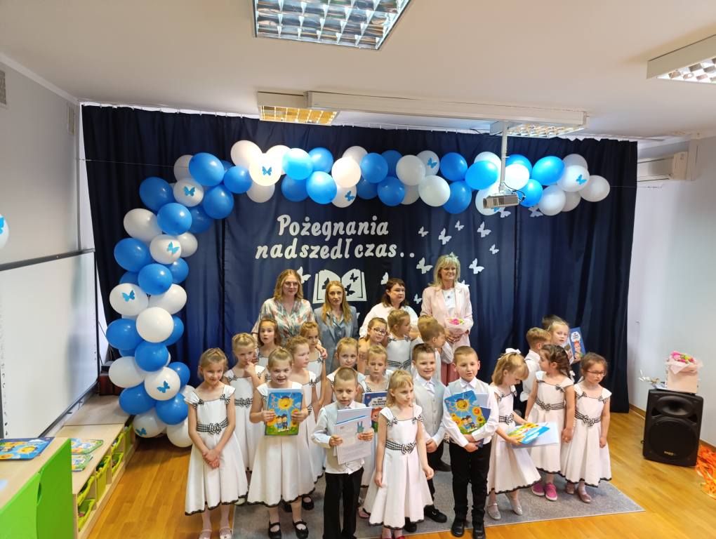 Dzieci ubrane na galowo stoją w grupie razem z Paniami i pozują do zdjęcia.