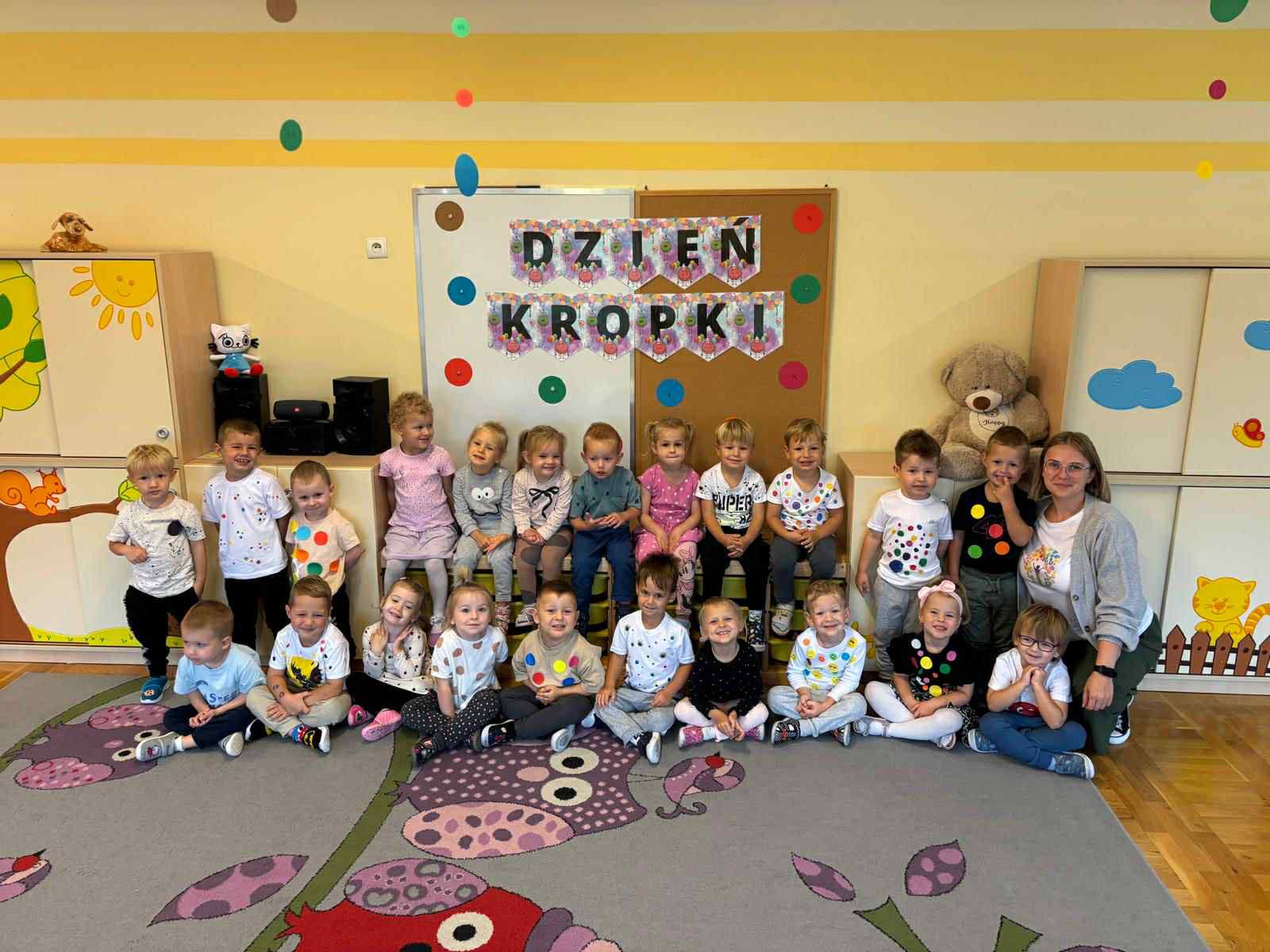 Dzieci ubrane w bluzeczki z kropkami pozują do zdjęcia razem z panią.