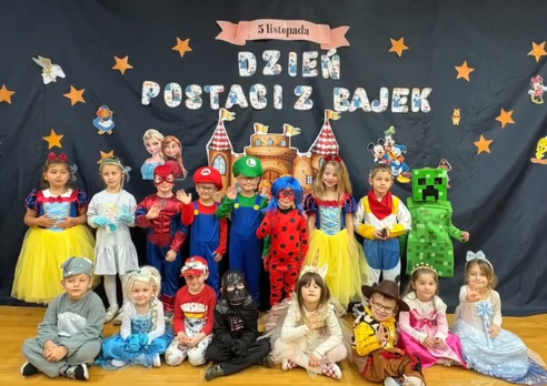 Dzieci przebrane za postacie z bajek pozują do zdjęcia na niebieskim tle z napisem dzień postaci z bajek.