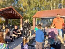 Rodzice pieką kiełbaski przy ognisku.