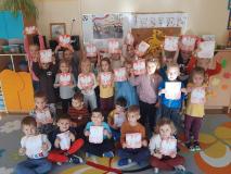 Dzieci stoją w grupie trzymając w rękach prace plastyczną godło polskie.