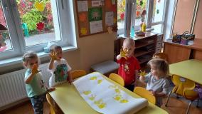 Dzieci odbijają ręce pomalowane na żółto na białej kartce.