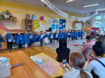 Dzieci stoją w półkolu ubrane w niebieskie pelerynki.