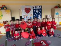 Dzieci ubrane na czerwono siedzą na dywanie w grupie.