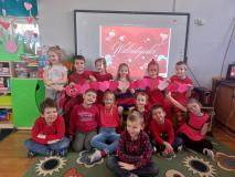 Dzieci ubrane na czerwono pozują do zdjęcia na tle walentynkowym.