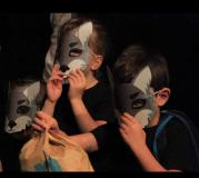 Dzieci siedzą na scenie w maskach zwierząt.