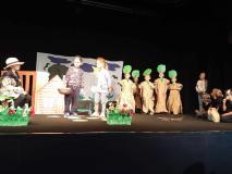 Dzieci przebrane za drzewa i zwierzęta stoją na scenie.