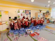 Dzieci ubrane na czerwono, trzymają w ręku paczki, pozują do zdjęcia z mikołajem.