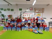 Dzieci ubrane na czerwono, trzymają w ręku paczki, pozują do zdjęcia z mikołajem.