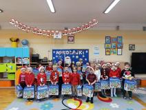 Dzieci ubrane na czerwono, trzymają w ręku paczki, pozują do zdjęcia z mikołajem.