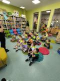 Dzieci siedzą na małych dywanikach w bibliotece.