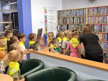 Dzieci oglądają książki znajdujące się na regałach w bibliotece.