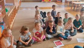 Dzieci siedzą w grupie na dywanie.