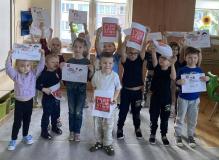 Dzieci stoją trzymając w rękach kartki z obrazkiem logo kampanii.