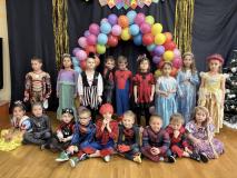 Dzieci przebrane za postacie z bajek stoją w grupie na tle łuku z balonów