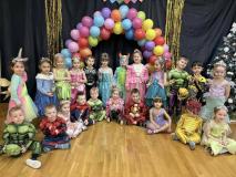 Dzieci przebrane za postacie z bajek stoją w grupie na tle łuku z balonów.