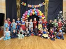 Dzieci przebrane za postacie z bajek stoją w grupie na tle łuku z balonów.