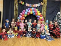 Dzieci przebrane za postacie z bajek stoją w grupie na tle łuku z balonów.