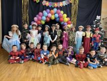 Dzieci przebrane za postacie z bajek stoją w grupie na tle łuku z balonów