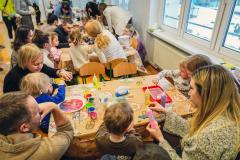 Dzieci wraz z rodzicami przy stolikach wykonują żółte słoneczka z papieru.